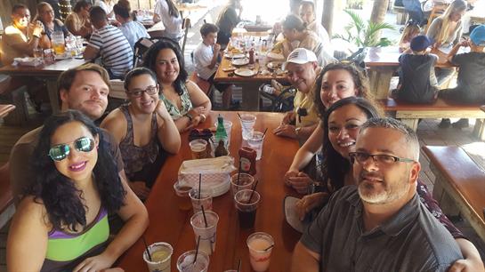 Friends smile and share food and drinks around a large table, creating joy.