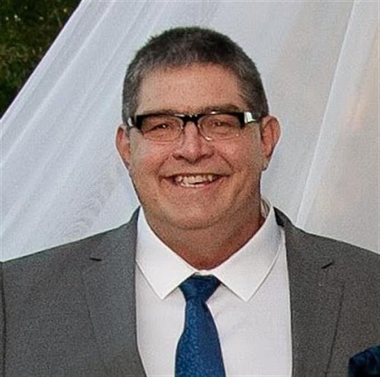 Smiling man wearing glasses and a suit enjoys a joyful moment at a garden event.