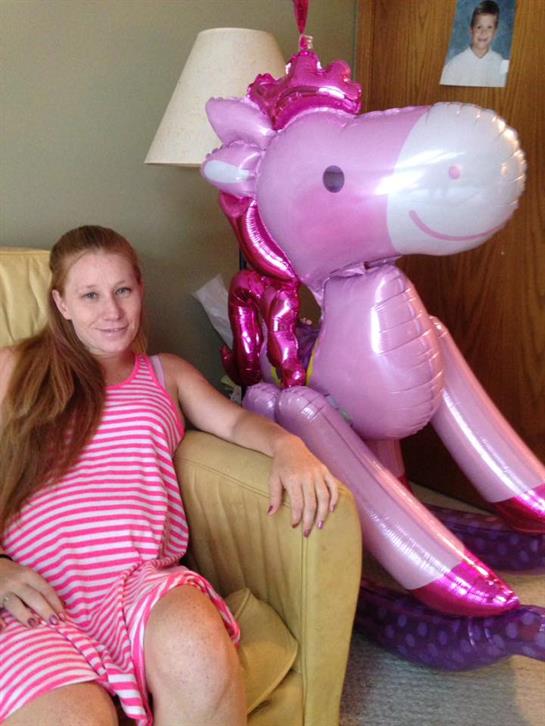 Young girl sits comfortably in a chair beside a colorful unicorn balloon, enjoying leisure time.
