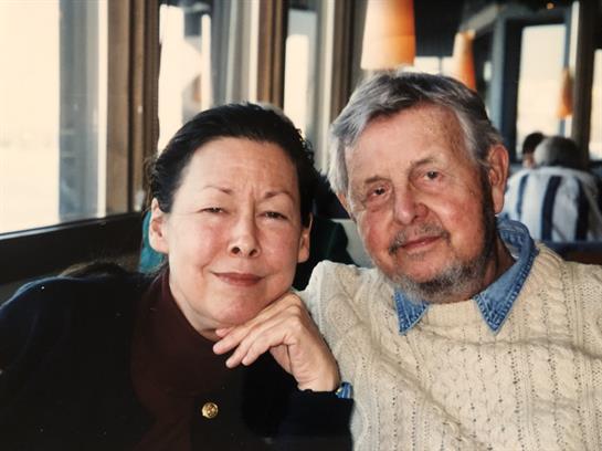 Two elderly individuals share a warm moment inside a cafe on a rainy day.