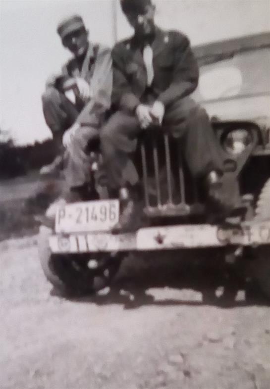 Two military personnel sit on a jeep, enjoying a peaceful afternoon in a natural setting.