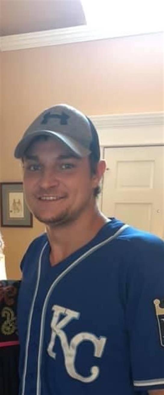 A man stands inside a home, smiling warmly while engaging with friends at a casual gathering.