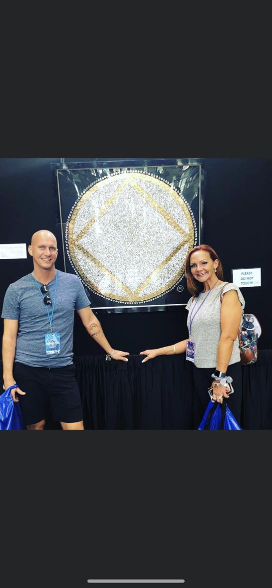 Two individuals engage with a large, colorful crystal artwork at an event in an indoor space.