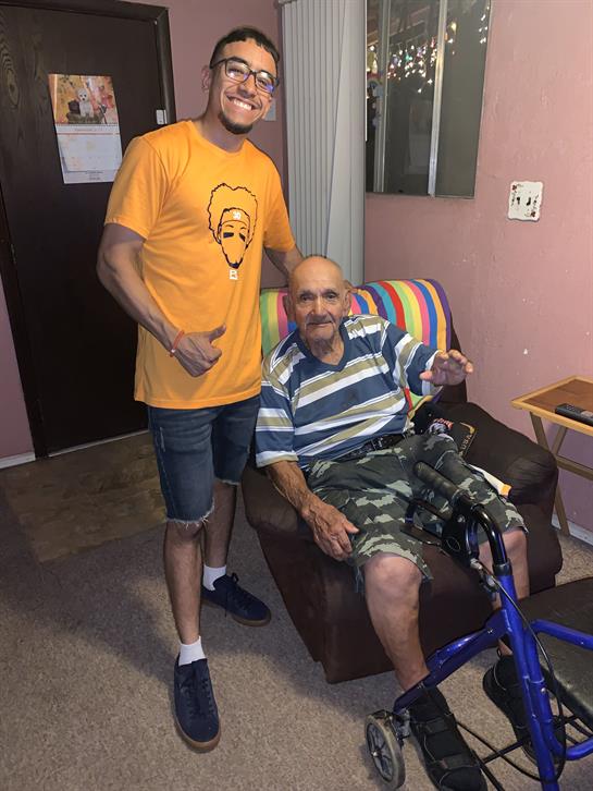 A young man poses with an elderly gentleman in a welcoming living area, highlighting their bond.