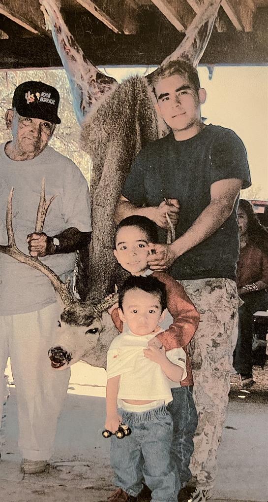 A group of individuals celebrates a successful hunt while posing with a deer in a forested area.