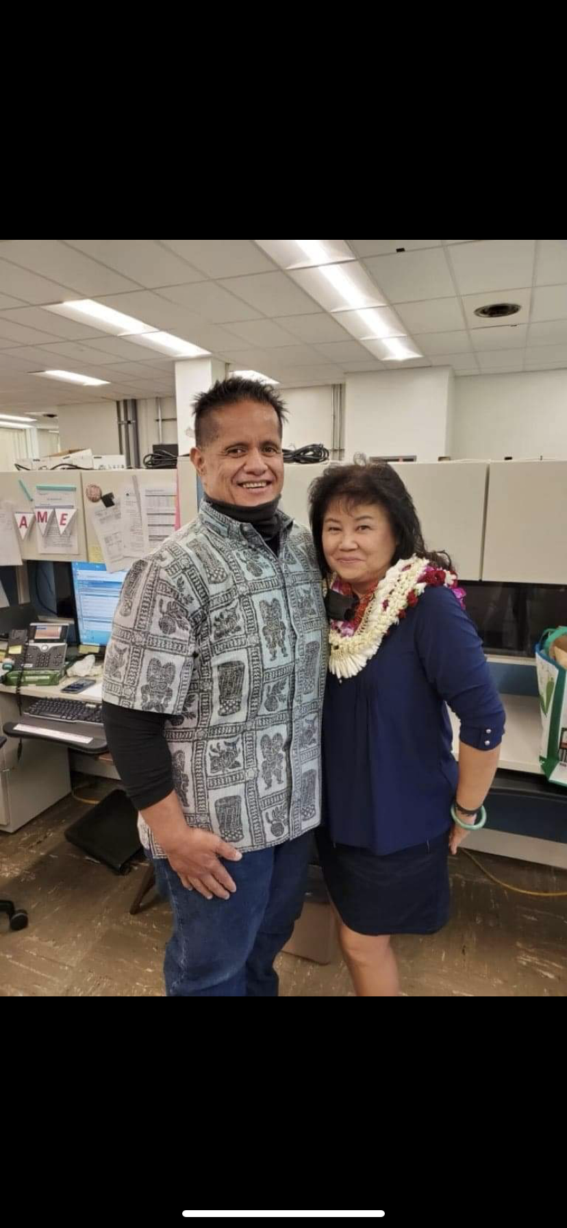 Two colleagues in traditional attire celebrate their friendship in an office environment with leis.