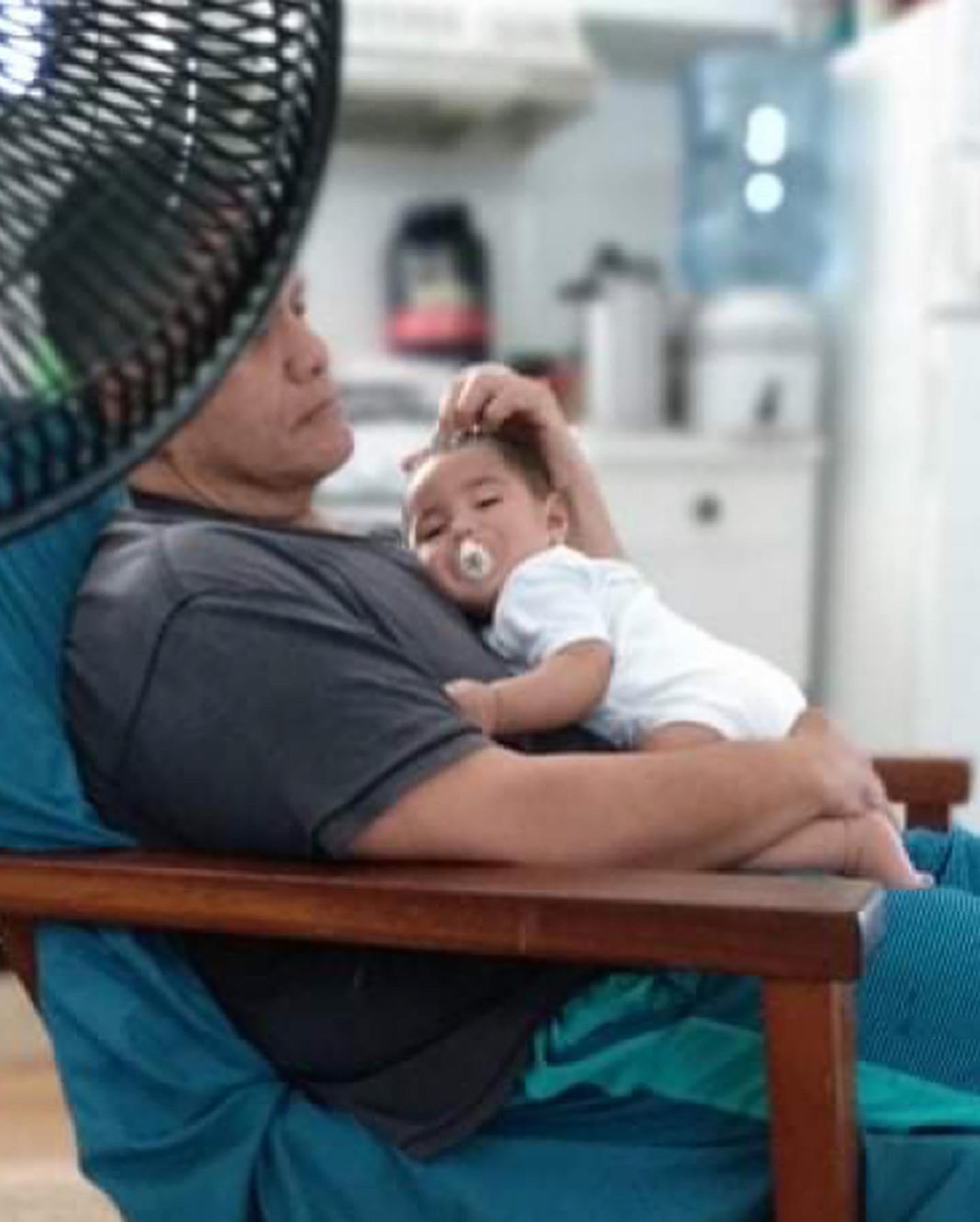 A father relaxes in a chair while holding his sleeping baby close in a cozy setting.