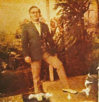 A man enjoys a relaxed moment in a lush garden, posing with one foot on a decorative ledge.