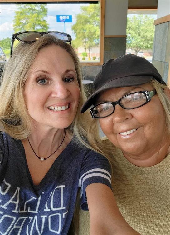 Two women smile and pose for a selfie at a local cafe, enjoying their time together during the day.