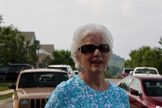 Senior woman enjoys the outdoors in a colorful outfit while standing among parked vehicles.