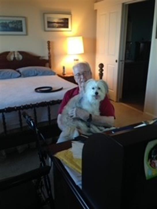 An elderly man enjoys the company of a small dog while seated in a cozy bedroom during the evening.