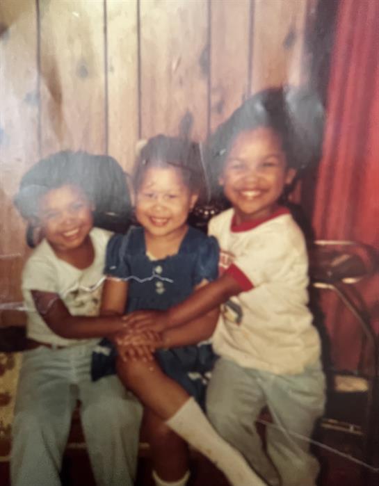 Three cheerful kids smile brightly while sitting closely together in a wooden room.
