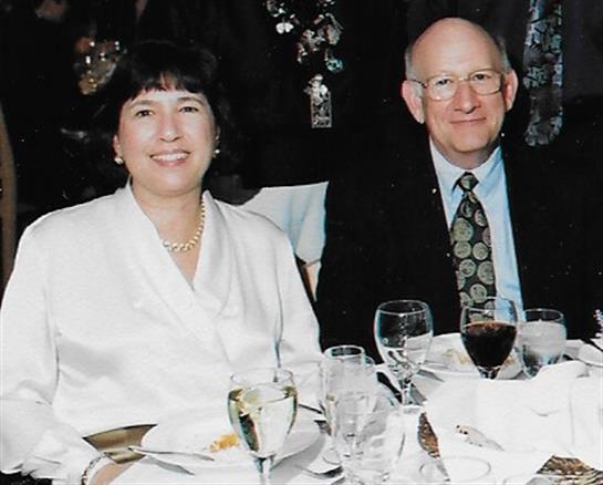 A couple smiles at a table with drinks and elegant dinnerware at an event.