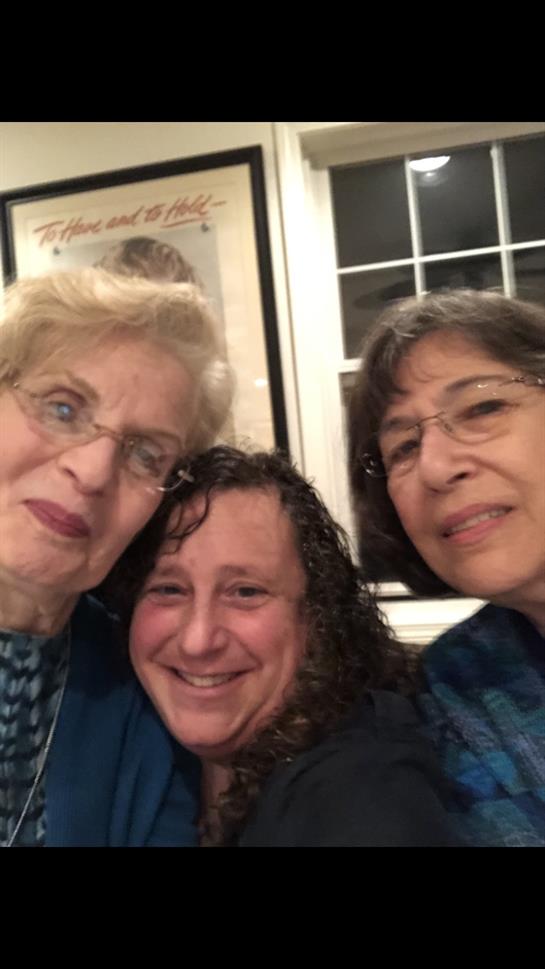 Women smile happily together, enjoying friendly conversation at an indoor social event.