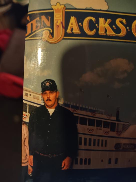 A man in a black uniform stands by a vintage riverboat at a sunset exhibition.
