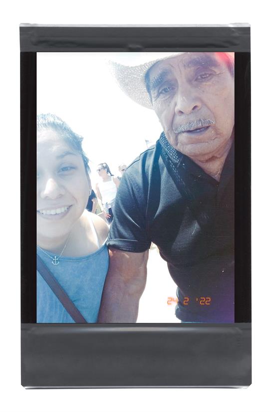 A young woman stands next to an elderly man, both smiling, during a lively outdoor gathering.