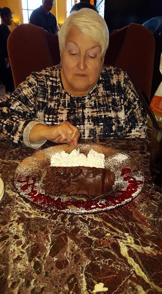 An elderly woman is savoring a rich chocolate dessert adorned with whipped cream.