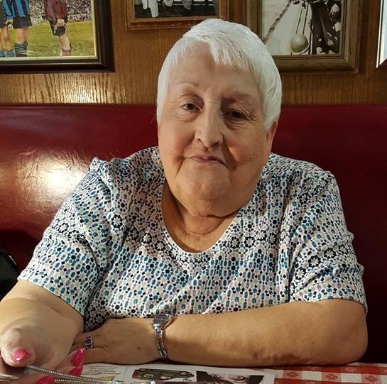 A senior woman happily sits in a red leather booth at a cozy diner.