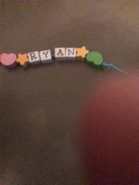 Beads arranged to spell Ryan’s name with colorful shapes on a dark surface during arts and crafts.