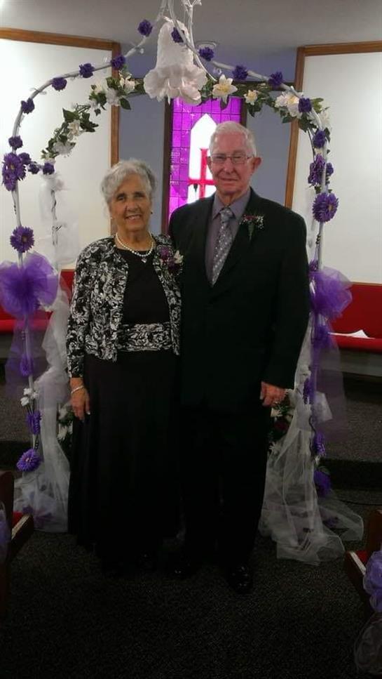 Elderly couple joyfully poses at their wedding anniversary celebration with decorations.