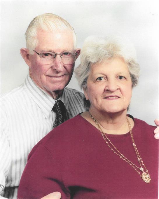 Older couple poses in a studio, smiling warmly at the camera, radiating affection and unity.