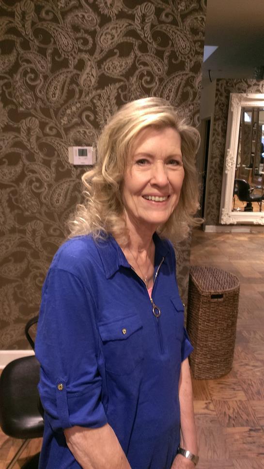 A cheerful woman with wavy hair sits in an elegant, textured room.