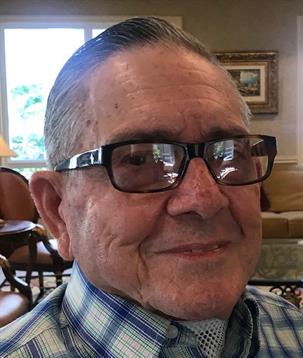 A cheerful elderly man with glasses enjoys a warm afternoon in a comfortable living space.