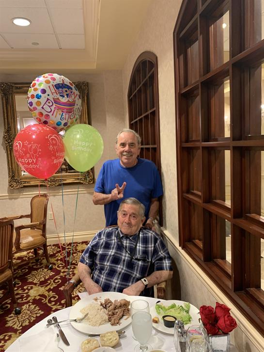 Two friends enjoy a celebration together, surrounded by balloons and a festive atmosphere.