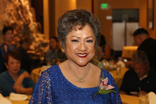 A woman smiles warmly while dressed in a blue formal outfit at a celebratory event with guests.
