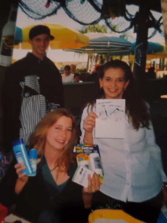 Two friends happily show off their prizes at a carnival filled with colorful tents.