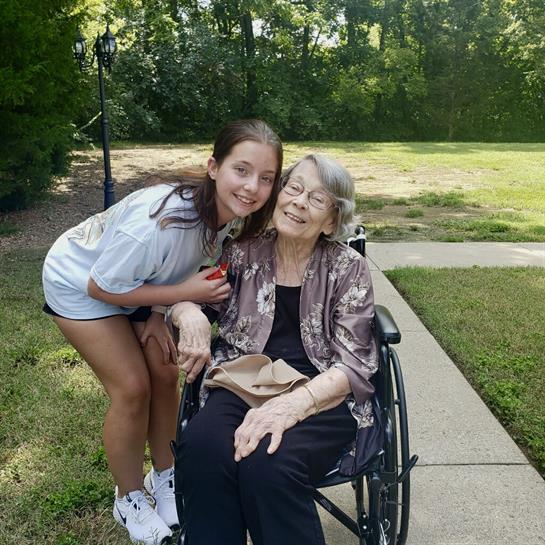 A girl smiles and hugs her grandmother in a park, showing their close bond and joy.