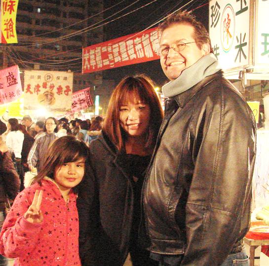 A family stands together at a lively night market, surrounded by colorful stalls and crowds.