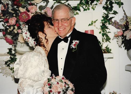 Bride kisses groom in elegant attire during a wedding ceremony decorated with flowers.