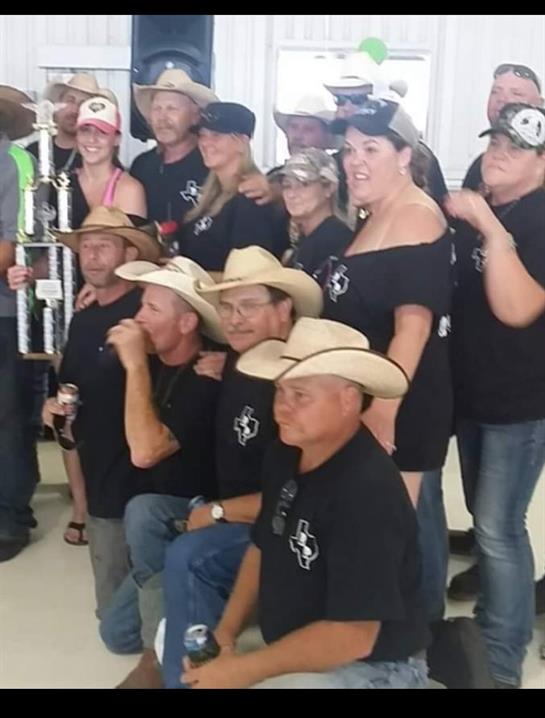 Friends posing joyfully in cowboy hats while holding a trophy in a bright indoor space.
