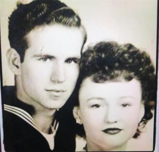 A young sailor in uniform and a woman stand closely together, smiling softly with vintage styling.
