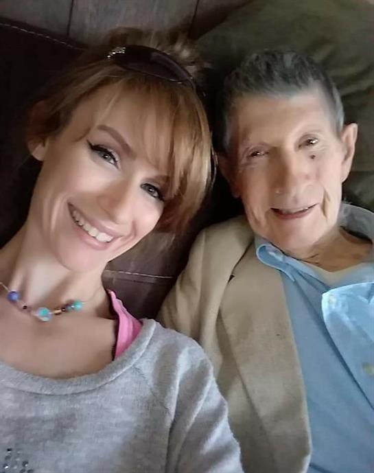 A woman and an elderly man are smiling together on a couch, enjoying each other's company.