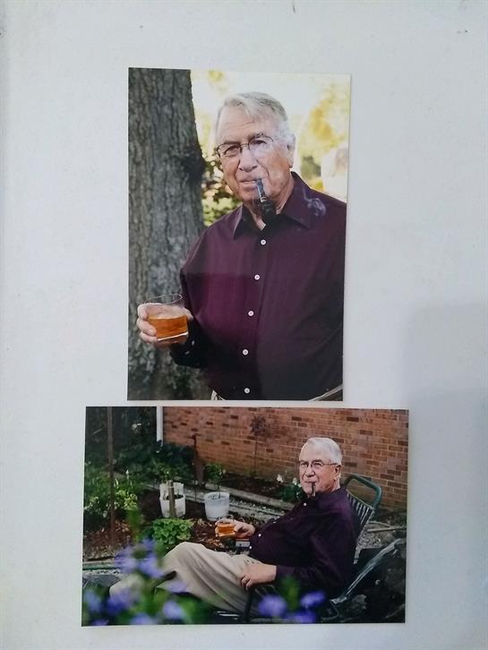 Elderly man holds a drink while relaxing outdoors in a peaceful garden setting.
