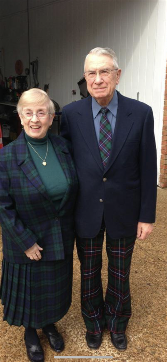 Two elderly individuals wear matching plaid attire while enjoying a social event outdoors.