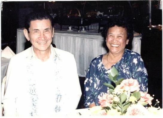 A smiling couple enjoys a lively moment together surrounded by floral decorations at a gathering.