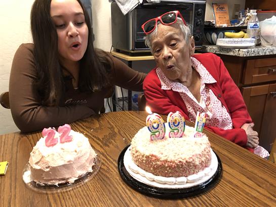 Family members celebrate two birthdays with joyful singing and cake in a warm kitchen setting.