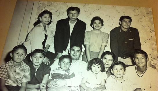 A diverse family poses together, smiling in unique outfits against a cozy backdrop.