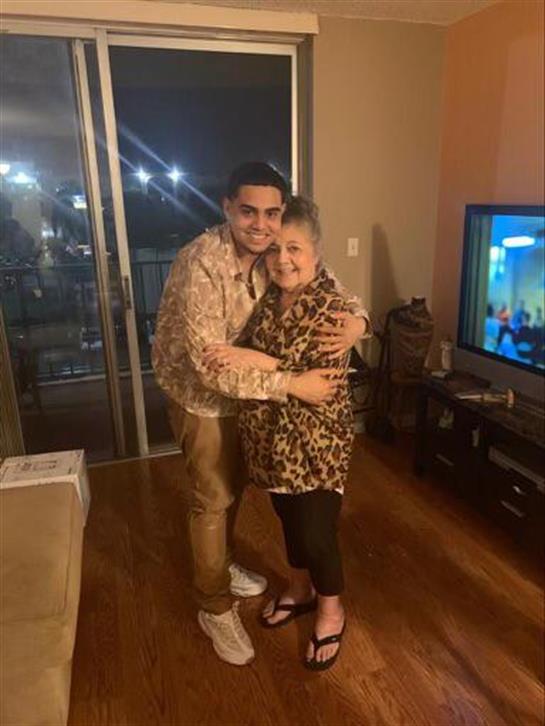 A man warmly embraces his grandmother in a well-lit living room during a family gathering.