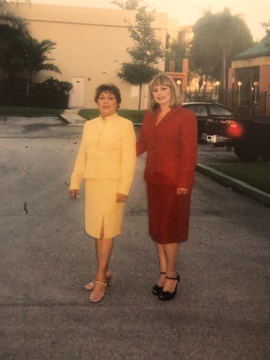 Two women stand side by side, smiling, in stylish suits on a warm afternoon.
