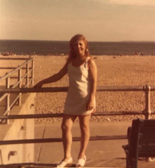 A young woman stands on the boardwalk, smiling and enjoying a sunny day by the beach.