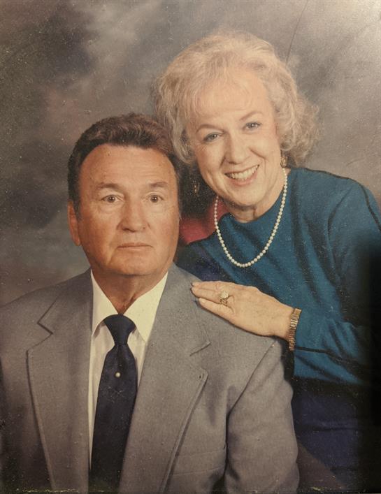 A senior couple enjoys a close moment, smiling together while dressed elegantly in a studio.
