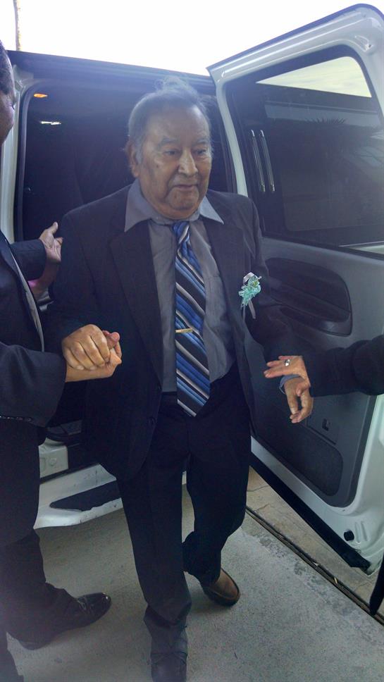 An elderly man is being helped out of a vehicle by two people in formal attire during the night.