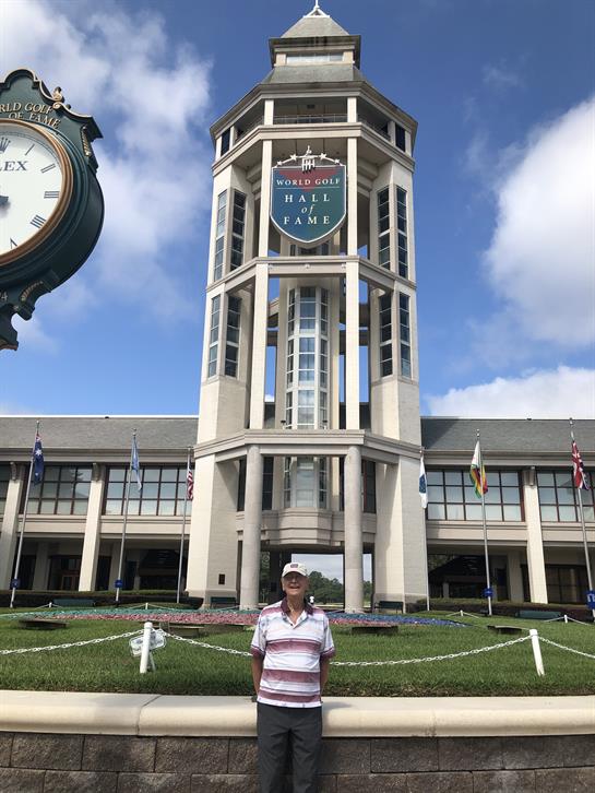 A visitor poses in front of the Hall of Fame building under a clear blue sky during the day.