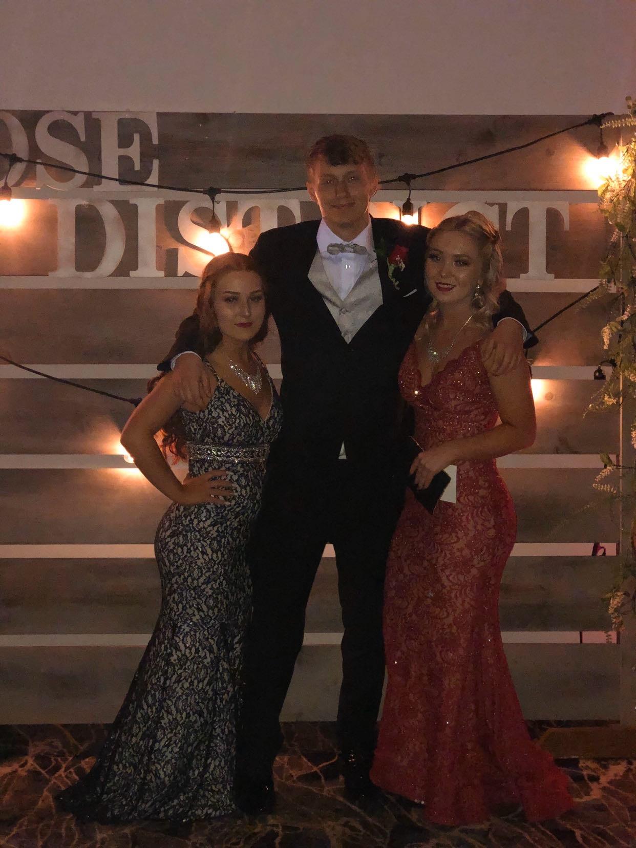 Three friends in elegant outfits smile together at a formal event.