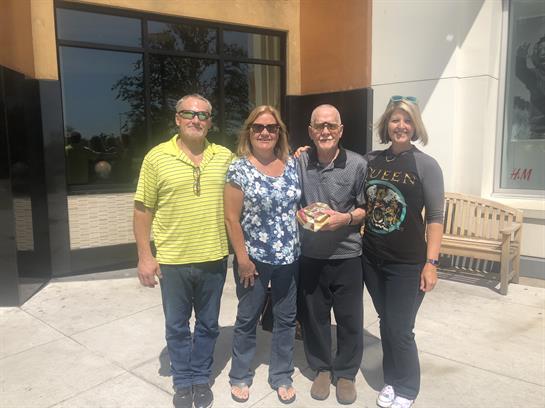 Group of four friends poses together outside a community building on a sunny afternoon.