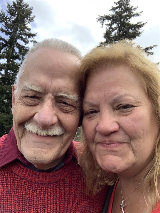 Two seniors share smiles and happiness in a beautiful outdoor setting surrounded by trees.